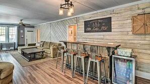 A cozy living room with a wooden floor, a sofa, a coffee table, and a bar area with stools and a refrigerator. - Forestport Home w/ Access to Otter Lake (Forestport)