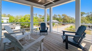 Eine überdachte Terrasse mit Adirondack-Stühlen und einem Tisch, mit Blick auf eine Wohngegend mit Bäumen und Häusern.