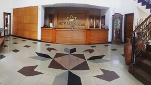 Et hotellets receptionområde med et gulv af geometriske fliser, en receptionsdisk med et kronelogo og en trappe til højre.