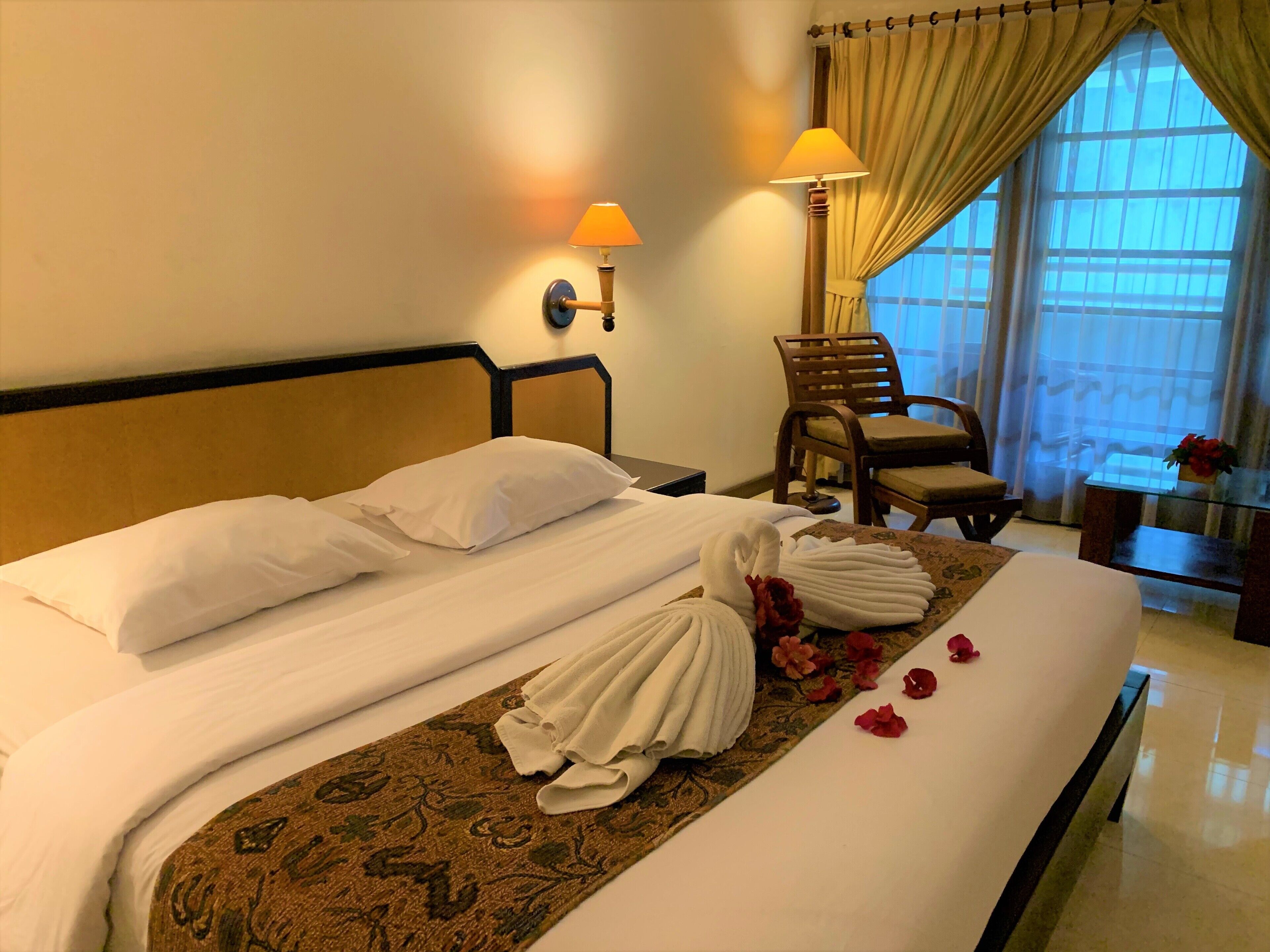 Una cama bien hecha con sábanas blancas, una alfombra estampada con motivos florales y un juego de toallas sobre la cama.