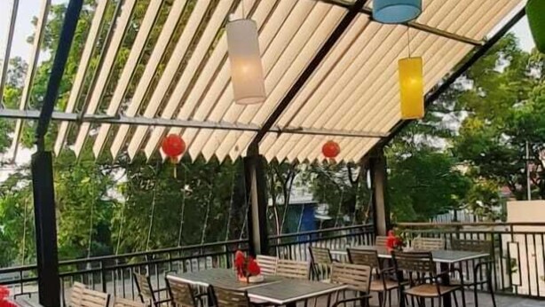 En udendørs patio med borde og stole, et træloft og hængende lamper.