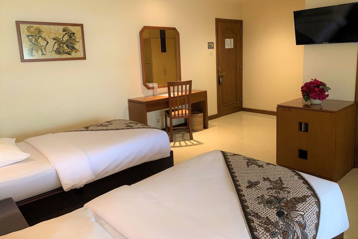 Een hotelkamer met twee bedden, een bureau met een stoel, een televisie en een spiegel.