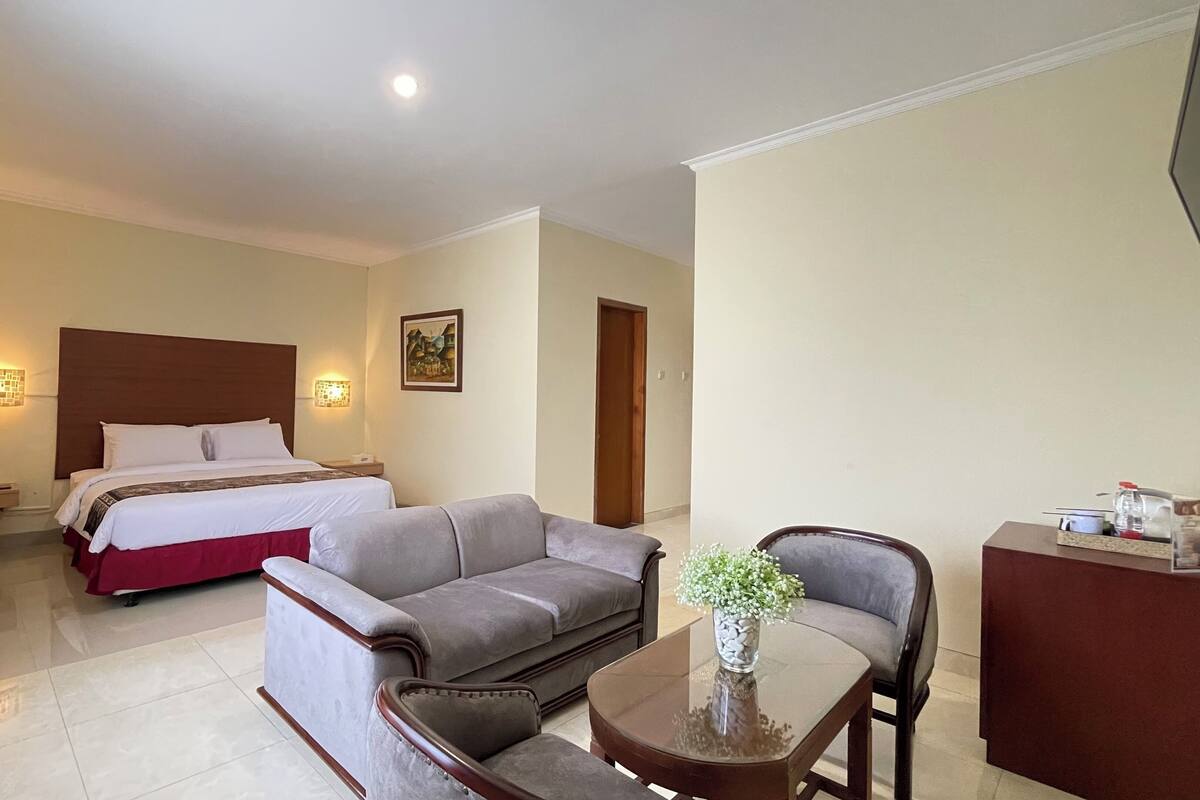 Een hotelkamer met een bed, een grijze bank, een kleine tafel met een vaas en een bureau met een fles en glaasjes.