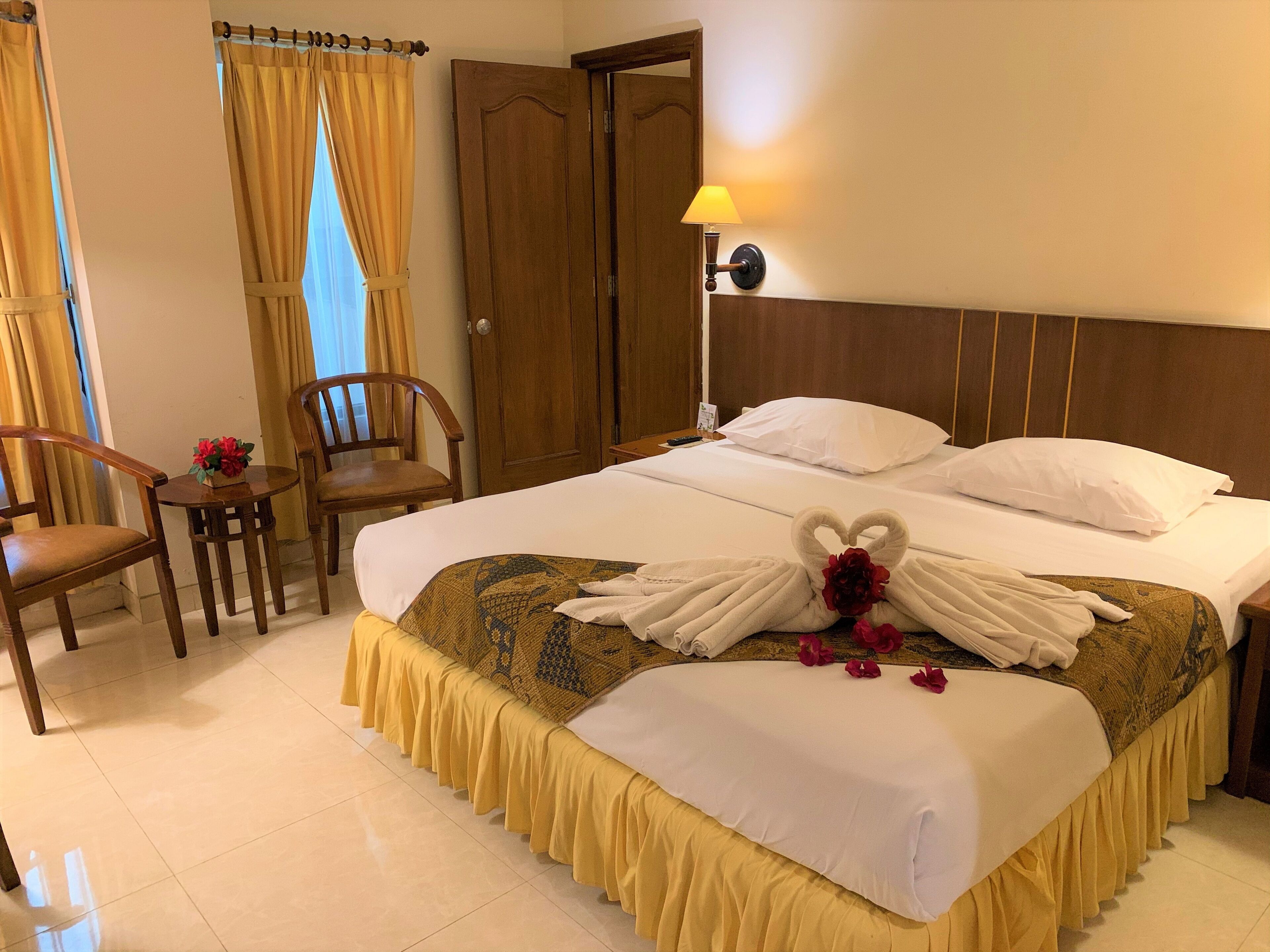 A hotel room with a neatly made bed, a small table with a chair, and a lamp.