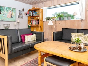 Una sala de estar acogedora con una mesa de madera, dos sofás negros, una estantería y una ventana con plantas.