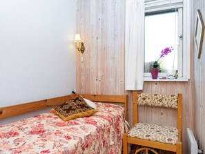 A small room with a bed, a chair, a window with a curtain, and a wall-mounted lamp.