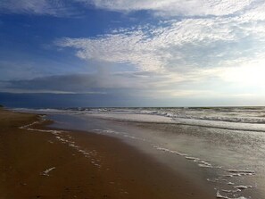Una playa con una amplia orilla arenosa y olas suaves.