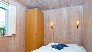 A room with a wooden wardrobe, a bed with white bedding, and two wall-mounted lamps. - 7 Person Holiday Home in Hvide Sande-by Traum (Hvide Sande)