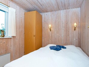 A room with a wooden wardrobe, a bed with white bedding, and two wall-mounted lamps.