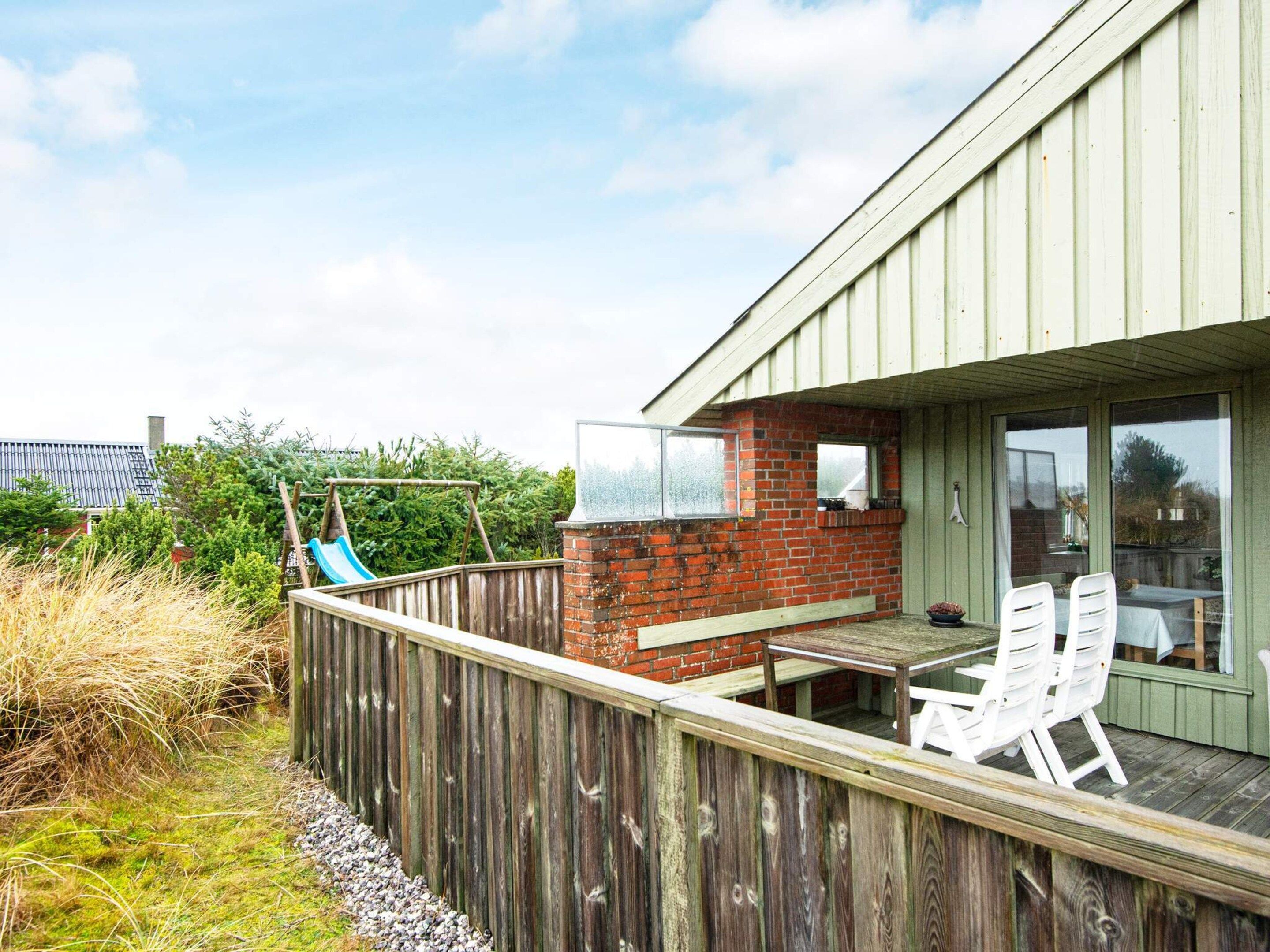 Une terrasse en bois avec une table et des chaises, un mur en briques et une balançoire.