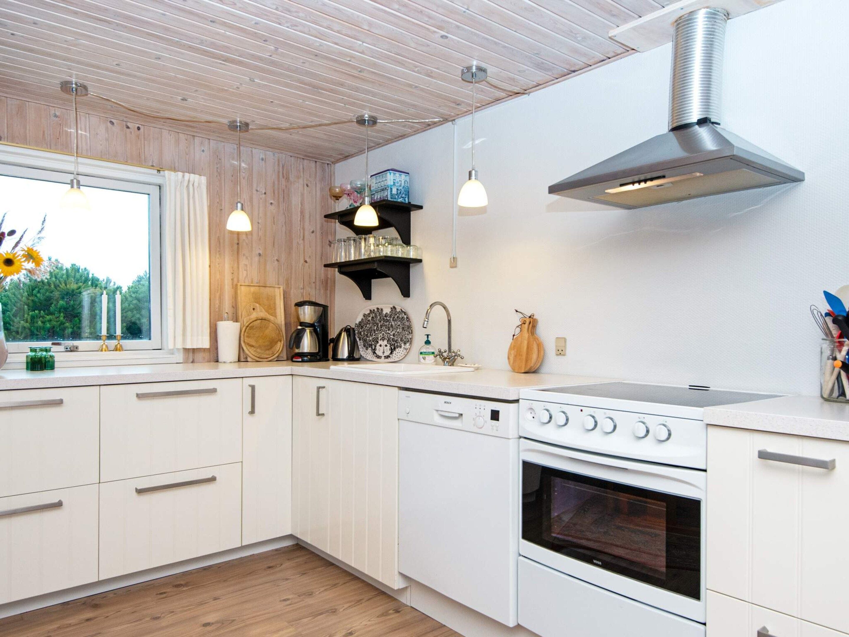 A modern kitchen with white cabinetry, a stainless steel range hood, a built-in oven, and pendant lighting.