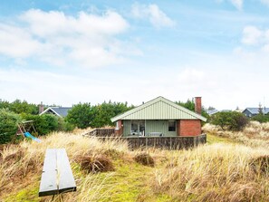 A single-story house with a green roof, surrounded by tall grass and trees.