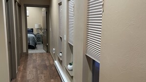 Un pasillo con piso de madera, paredes beige y varias ventanas con persianas.