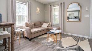 Una sala de estar moderna con un sofá color beige, dos mesitas redondas, un espejo grande y una alfombra estampada.