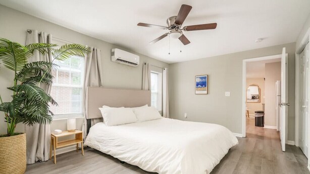 Un dormitorio con una cama, ventilador de techo, planta en maceta, mesita de noche y ventana con cortinas.