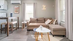 Una sala de estar moderna con un sofá, una mesita y una cocina con aire acondicionado y microondas.