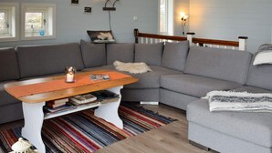 Een moderne woonkamer met een grijze hoekbank, een houten salontafel en een kleurrijk gestreept tapijt.