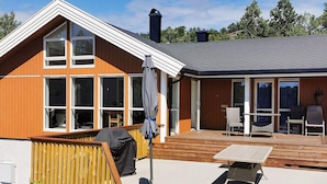 Een tweelaags huis met een terras, grote ramen en tuinmeubilair.