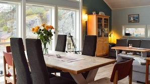 Een eetgedeelte met een houten tafel, zwarte stoelen met bekleding en een vaas oranje bloemen.