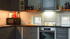Een keuken met grijze kastjes, een magnetron, een oven en een raam met uitzicht op bomen.