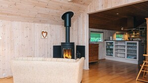A cozy living room with a wood-burning stove, a sofa, and a kitchen area with shelves and a window. - 6 Person Holiday Home in Glesborg-by Traum (Glesborg)