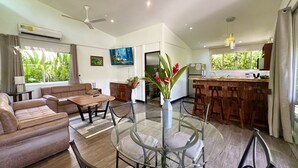 Ein modernes Wohnzimmer mit Glastisch, Sofas und einer Küchenzeile mit Bar.
