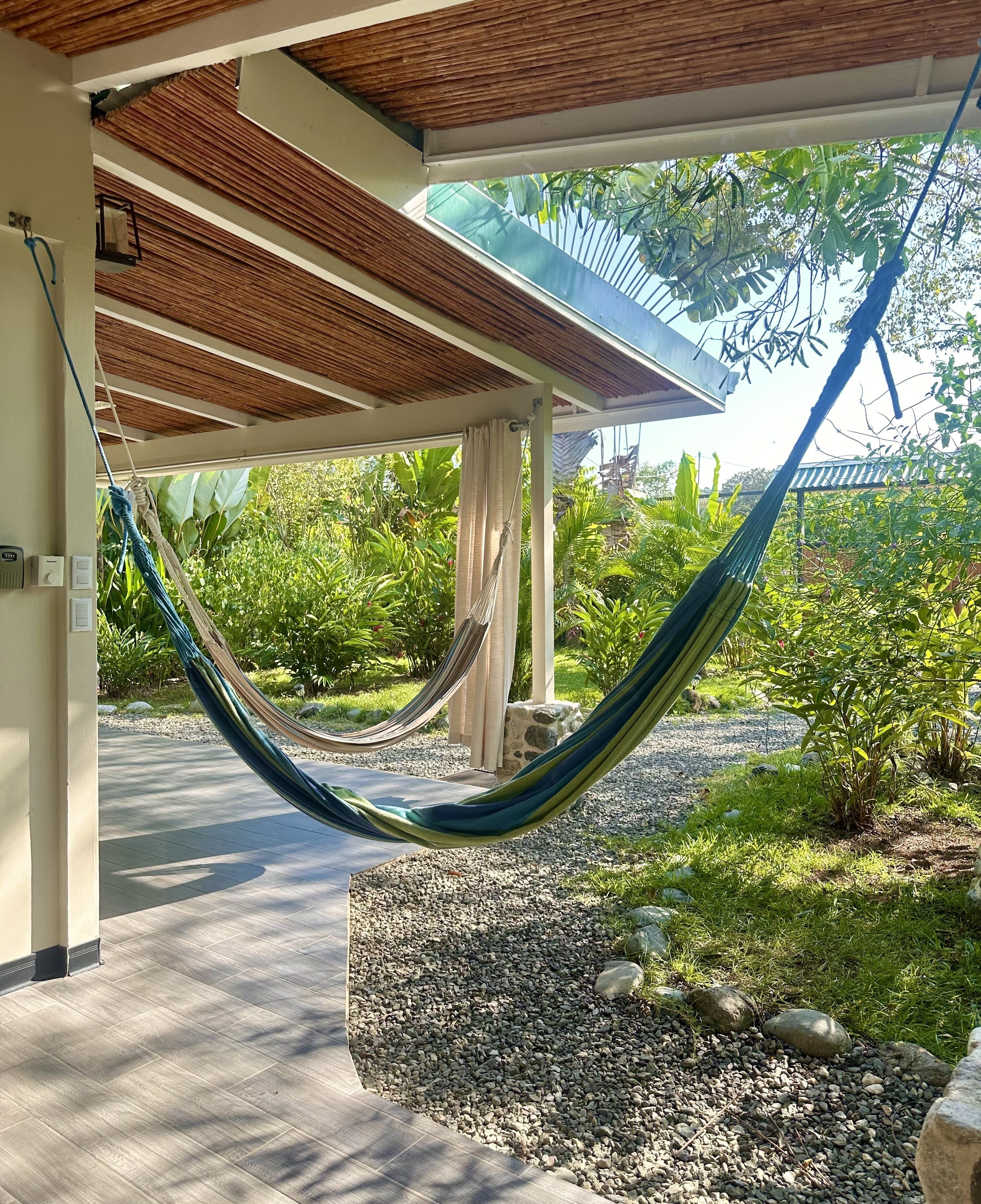 Un hamac installé dans un espace abrité, avec vue sur un jardin et un sentier.