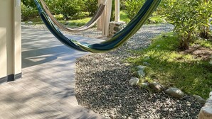 Eine Hängematte unter einem Überdachung mit Blick auf einen Garten und einen Weg.