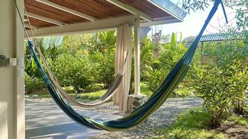 Un hamac installé dans un espace abrité, avec vue sur un jardin et un sentier.