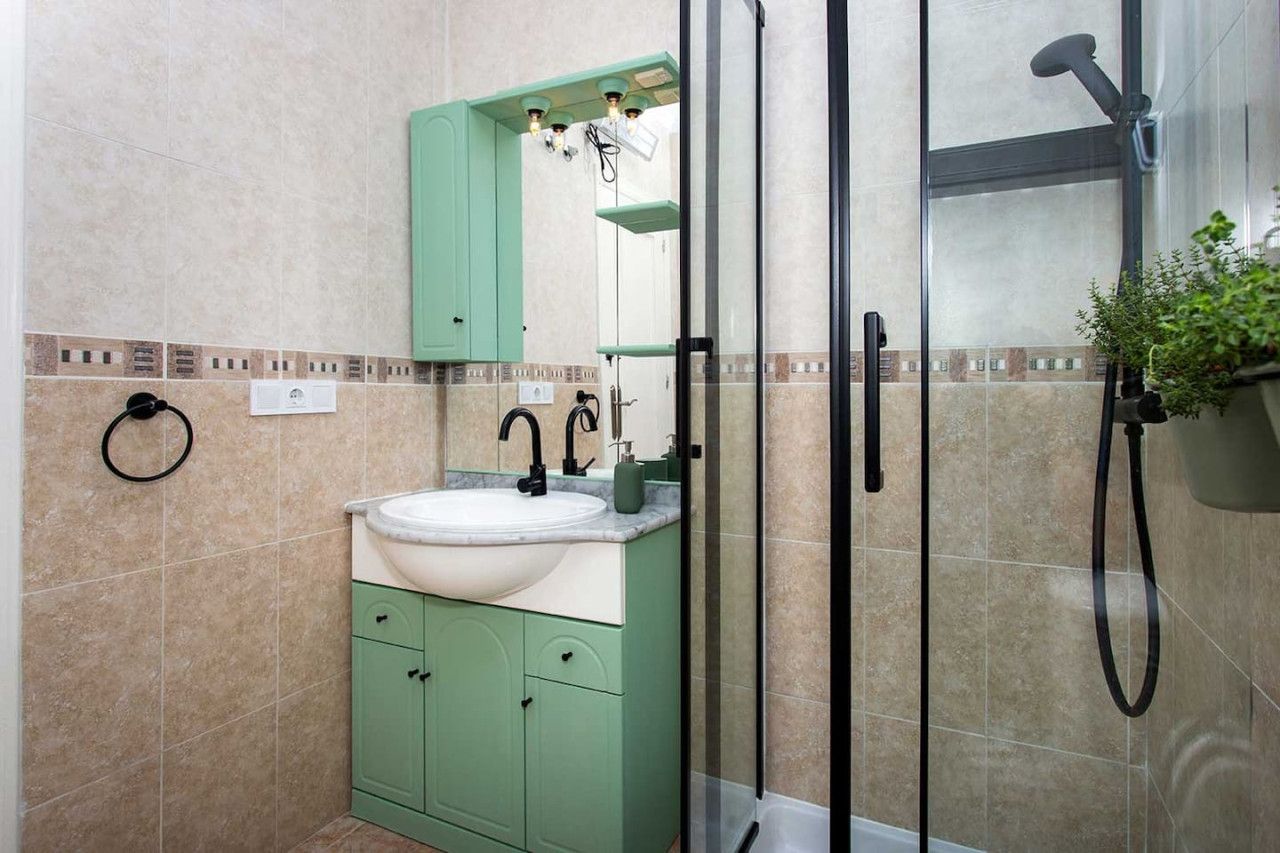 Un baño con lavamanos, espejo, muebles verdes y zona de ducha.