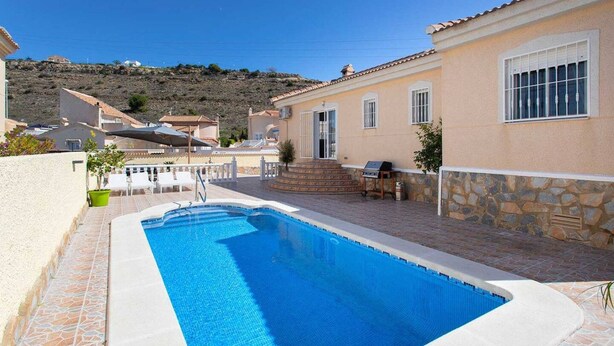 Uma piscina com borda de pedra, uma parede de pedra e vista para casas ao fundo.