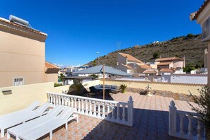 A terrace with lounge chairs, a table, and umbrellas, overlooking a hillside with buildings. - CH Villa Rio Mundo Rojales (Rojales)