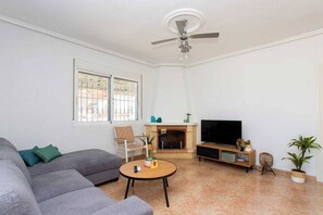 Un salon comprenant un canapé, une table basse, une cheminée, un téléviseur et un ventilateur de plafond.