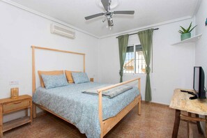 A bedroom with a bed, a ceiling fan, a window with curtains, a television on a stand, and a small plant on a shelf. - CH Villa Rio Mundo Rojales (Rojales)