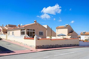 A residential building with a red-tiled roof, a stone wall, and a clear blue sky.