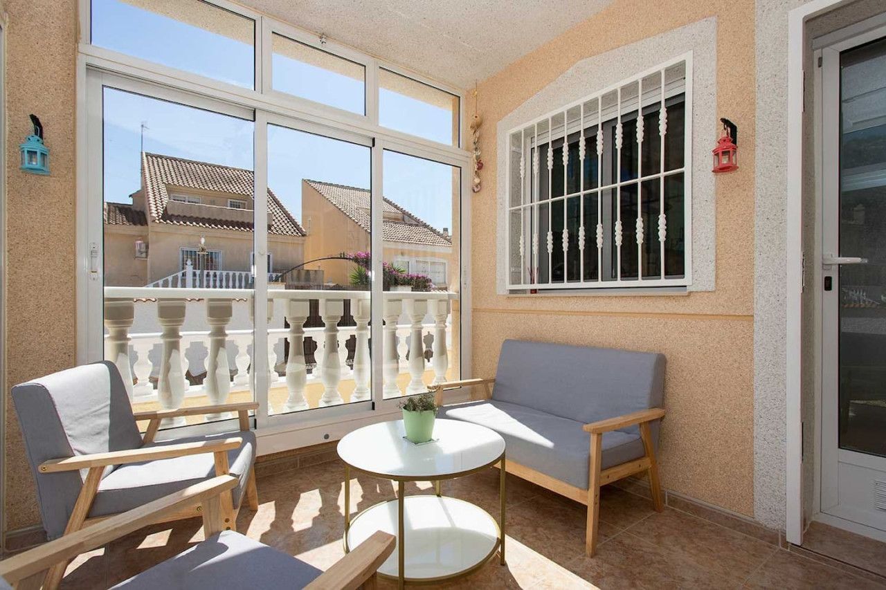 A sunlit balcony with a white railing, a grey sofa, and a small round table.