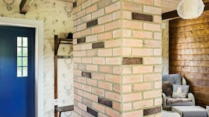 A room with a brick wall, a blue door, wicker furniture, and a wooden ceiling. - 5 Star Holiday Home in Odensvi (Gamleby)