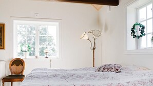 A bedroom with a large bed, a chair, a floor lamp, and a window with a view of trees. - 5 Star Holiday Home in Odensvi (Gamleby)