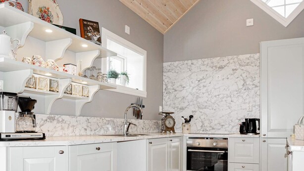 A kitchen with white cabinetry, a marble backsplash, a built-in oven, and a window above the sink. - 5 Star Holiday Home in Odensvi (Gamleby)