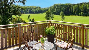 A wooden deck with two wicker chairs and a glass table, overlooking a green field and forest. - 5 Star Holiday Home in Odensvi (Gamleby)