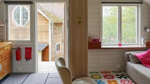 A cozy attic bedroom with a sloped ceiling, wooden walls, a window with a view of trees, a colorful rug, and a small shelf with items. - 2 Person Holiday Home in Haninge-by Traum (Tyreso)