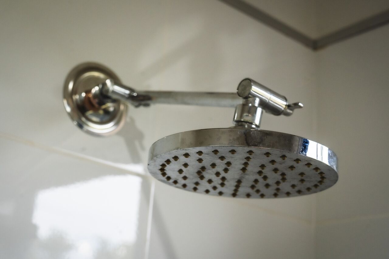 A showerhead with a round, perforated design, mounted on a wall with a metallic finish.
