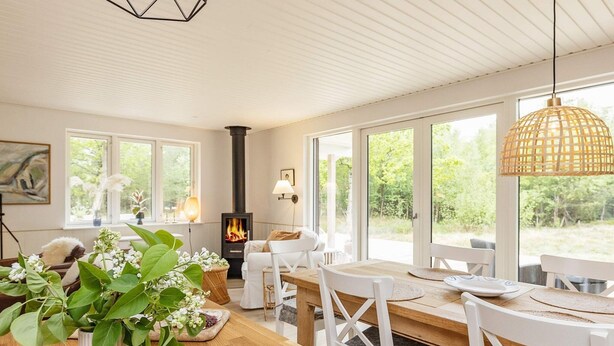Un coin repas accueillant avec une table en bois, des chaises blanches et une grande fenêtre donnant sur un paysage verdoyant.