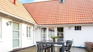 En täckt uteplats med ett bord och stolar, en krukväxt och en vattenslang på däckytan.