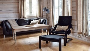 L’intérieur d’une cabane en rondins, avec un plancher en bois, un canapé en cuir noir, une table basse en bois, un fauteuil noir et un lampadaire.