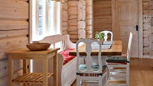 L’intérieur d’une cabane en rondins, avec une table en bois, une chaise, un lit avec des oreillers et une fenêtre avec des rideaux.