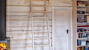 Un intérieur en bois avec une cheminée, une échelle en bois et une bibliothèque remplie de jeux de société.
