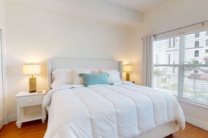 A bedroom with a large bed, two bedside tables with lamps, and a window with blinds.