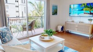 Una sala de estar con balcón, un televisor de pantalla plana y un mueble de mimbre.