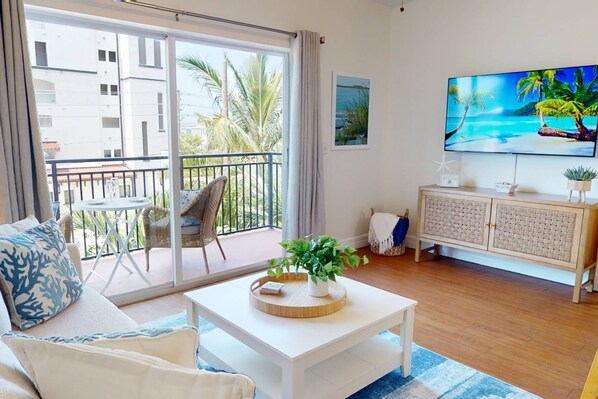 Una sala de estar con balcón, un televisor de pantalla plana y un mueble de mimbre.
